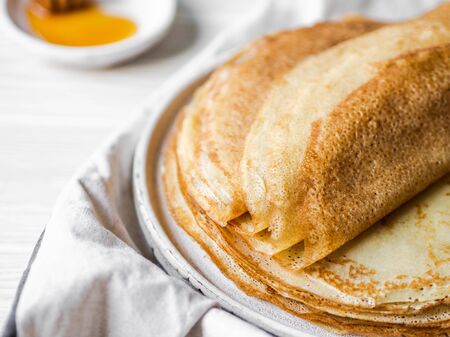 Stack Russian homemade thin pancakes on a white plate and wood honey spoon and honey on small white plate.の写真素材