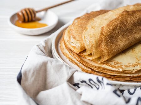 Stack Russian homemade thin pancakes on white plate and wood honey spoon and honey on small white plate. Traditional wheat pancakes for Shrovetide.の写真素材