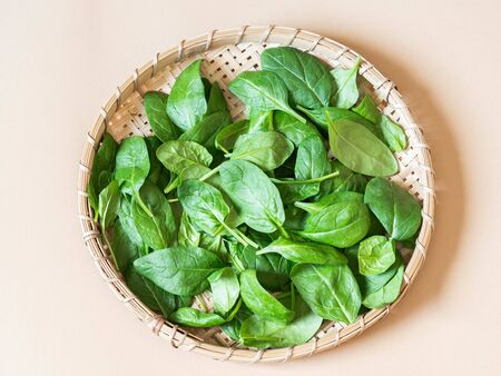 Wooden wicker tray with fresh spinach on light background. Top view.の写真素材