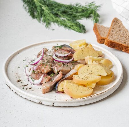 Marinated Herring fish with potatoes slices and red onion, rye bread on the a white table.の写真素材