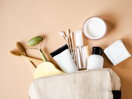 Travel cosmetic bag with the necessary means to care for women's skin. Cosmetics, massager with crystals, dry shampoo, cotton buds, toothbrushes in a cosmetic bag on a beige background. top viewの写真素材
