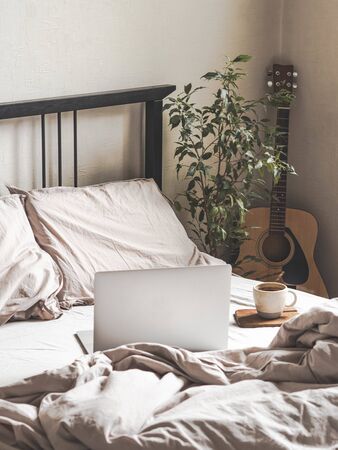 Laptop and coffee on the bed and a guitar next to the bed in the bedroom. Work from home or a comfortable pastime online. Stay home, quarantine. Work at home concept.の写真素材