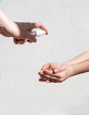 Hand treatment with sanitizer. Sanitizer in a bottle in the hands of an adult sprays on the substituted palms of the child on white background. copy spaceの写真素材