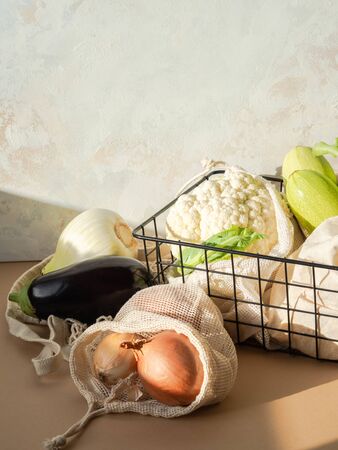 Various fresh vegetables in cloth reusable bags and a metal black basket in the sun on kitchen tableの写真素材