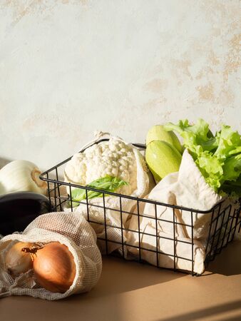 Various fresh vegetables in cloth reusable bags and a metal black basket in the sun on kitchen tableの写真素材