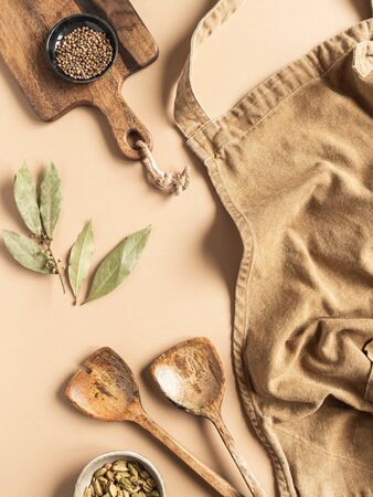 Kitchen flat lay of beige apron, small bowls with spices, wood kitchen utensils on a beigeの写真素材