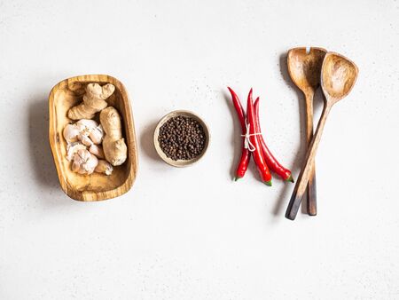 Flat lay of garlic in wood bowl, black pepper in bowl, red chili and wood spoon on a light background. top view. Copy spaceの写真素材
