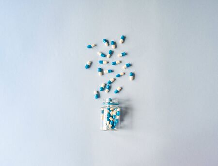 Medical therapeutic dissolving capsules of white and blue colors scattered out of the container on a blue background. Top view. Copy spaceの写真素材