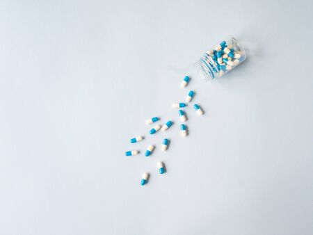 Medical therapeutic dissolving capsules of white and blue colors scattered out of the container on a blue background. Top view. Copy spaceの写真素材