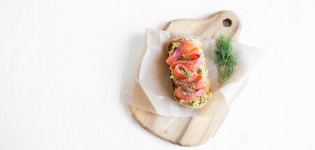 Avocado and smoked salmon toast on the white papper on wood board. Healthy food banner. Top view. Copy spaceの写真素材