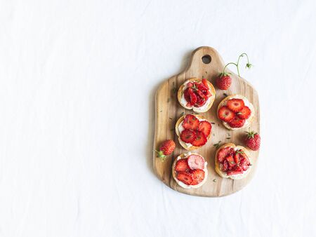 Toasts with red fresh strawberries, cream cheese and fresh thyme on wood board on a white background. top view. Copy spaceの写真素材