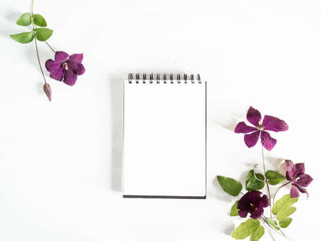 Flat lay composition of purple clematis flowers and leaves and notepad with a blank sheet layout on white background. Top view. copy spaceの写真素材