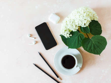Home office desk workspace with black smartphone, black coffee in cup, white hydrangea, white earphones and graphite pencils on pink background. Flat lay, top view girl work business concept for lifestyle blogの写真素材