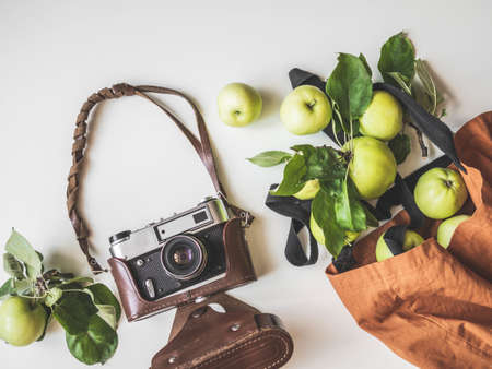 Fresh green apples with leaves in cotton brown bag and retro camera on white background. Top view....