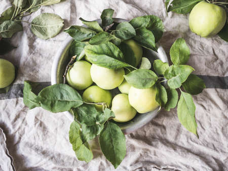 Metal bowl with green apples and leaves on a gray vintage linen napkin. Wallpaper of fruits.Top view, flat lay.の写真素材