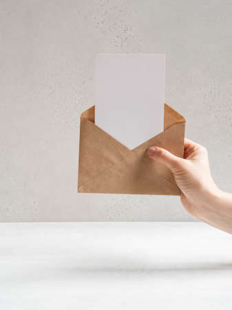 Female hand hold open kraft envelope and postcard on the gray background, front view. Copy space