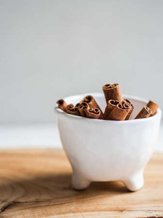 White ceramic bowl with cinnamon sticks on a wooden table on a white background. Front view. copy spaceの写真素材