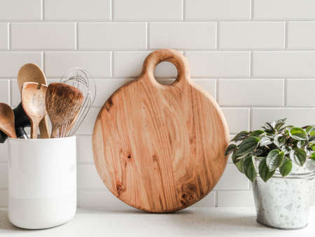 Stylish white kitchen background with kitchen utensils and wood cutting board for text on white countertop, copy space, front viewの写真素材