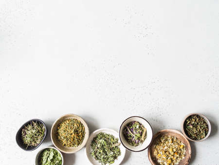 Various dry healthy herbs, plant flowers for brewing herbal tea in bowls on gray background. Top view. Copy spaceの写真素材