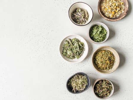 Various dry healthy herbs, plant flowers for brewing herbal tea in bowls on gray background. Top...