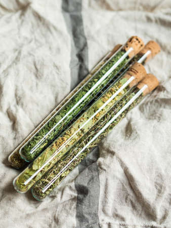 Glass test tubes with dry green herbal ingredients on dark background. Top view copy spaceの写真素材