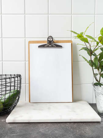 Stylish white kitchen background with basket with avocado, laurel plant in pot and clipboard with...