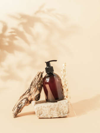 Stone podium and brown cosmetic bottle in creative composition on beige background with plant shadows. Copy space. Front viewの写真素材