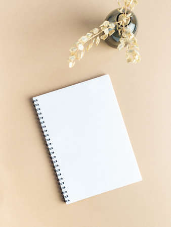 White blank notepad sheet with spiral and glass vase with dry plants on beige backgroundの写真素材