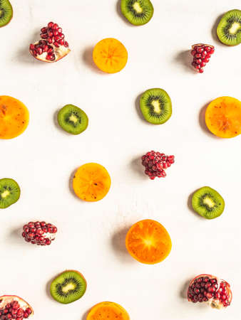 Multicolored seasonal healthy natural fruit background with persimmon, kiwi, pomegranate slices on white background. top view. Flat layの写真素材