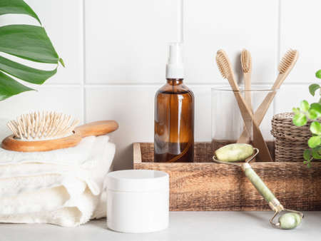White bath background front view with cosmetic bottle, bath accessories and green leaf on white shelf and wall tiles,の写真素材