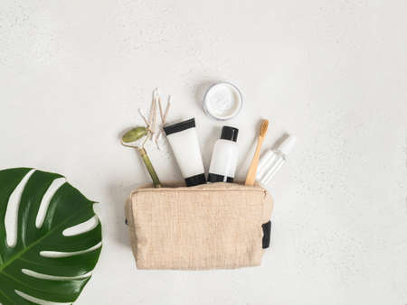 Eco travel cosmetic bag with the necessary means to care for women's skin. Cosmetics, massager with crystals, dry shampoo, cotton buds, toothbrushes in a cosmetic bag on gray background. top viewの写真素材