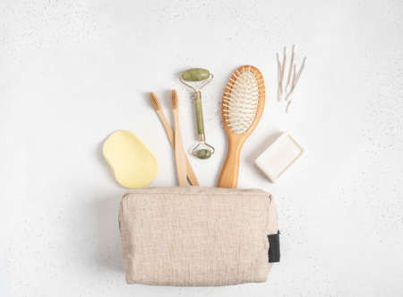 Eco cosmetic bag with a set of items for the care and hygiene of women. Bamboo toothbrush, comb, crystal massager, cotton swabs and soap on gray background. Flat lay. copy space. top view.の写真素材