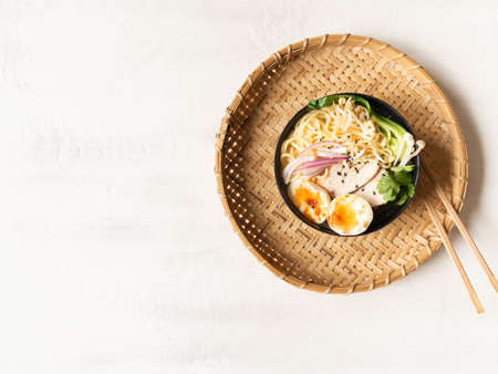 Chicken ramen noodle soup with meat, bok choy, mushrooms, egg in black bowl on gray background. Top view. copy spaceの写真素材