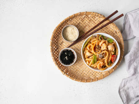 Udon noodles with seafood and vegetables cooked in a wok in a white bowl on a wicker tray. Top view. Copy spaceの写真素材