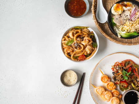Set asian food - ramen soup, grilled shrimp, stir fry vegetables and udon with seafood on a white background. Top view. Copy space. Flat layの写真素材