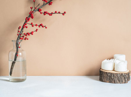 Winter home decoration with candles and branch with red berries in vase on beige background. Christmas minimal decoration concept. Front view, Copy spaceの写真素材