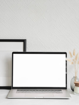 Laptop empty screen and different decoration against the white wall. Stylish home office. Front view. Copy spaceの写真素材
