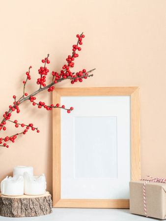 Ilex verticillata branches in vintage brown glass bottle, gift, candles and wood blank frame mock up on beige wall background. Front view. Copy spaceの写真素材