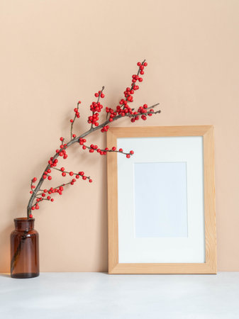 Ilex verticillata branches in vintage brown glass bottle and wood blank frame mock up on beige wall background. Front view. Copy spaceの写真素材