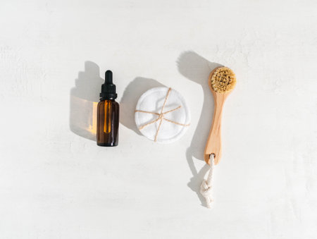 Brown glass bottle with dropper, reusable cotton pads and wooden facial brush on white backgroundの写真素材