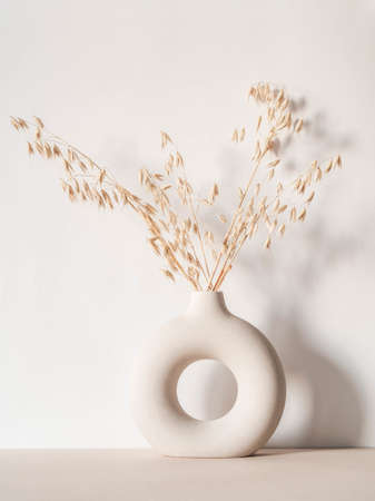 Round stylish ceramic vase with dried oats plant casting shadows on the wall. Front view. Copy spaceの写真素材