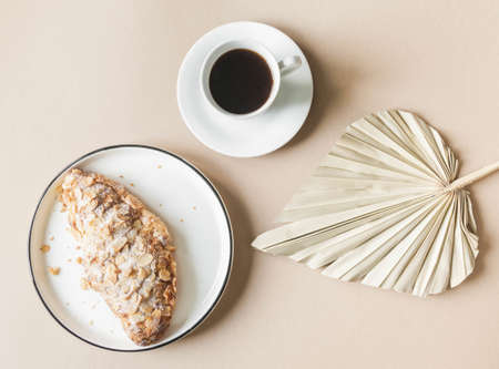 Cup of coffee with fresh croissant on white plate on beige background. Top view. Copy spaceの写真素材