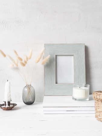 Modern still life of white dry lagurus flower in glass vase and various items on stack of white magazines on light background. Front view. Copy spaceの写真素材