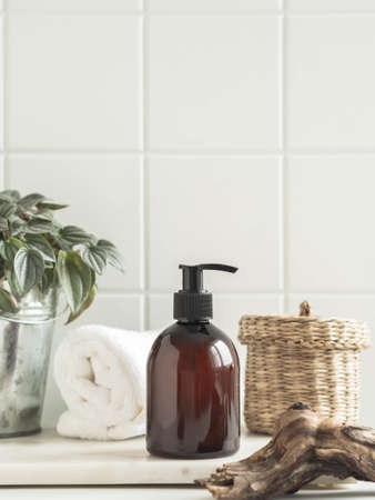 Plant, piece of wood and brown cosmetic bottle in creative natural composition on white tile background. Copy space. Front view. Product mock upの写真素材