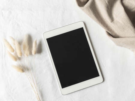 Empty black screen tablet mock up and fluffy dried flowers on white textured background. Flat lay. Top view. Copy spaceの写真素材