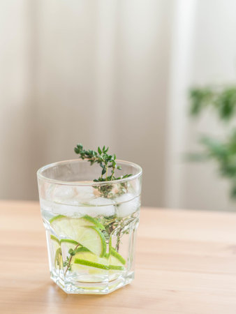 Summer homemade refreshing drink with lime, ice cubes and thyme on wooden background. Front view. Copy spaceの写真素材