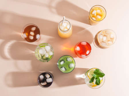 Various refreshing non-alcoholic drinks in glasses with ice. Different juice, homemade lemonade, iced coffee, iced fruit tea and smoothies on beige background. Copy space. top viewの写真素材