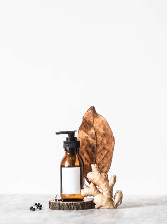 Creative trendy composition from brown cosmetic glass bottle with white label and various natural ingredients on white background. Front view. copy space. Blogging minimal beauty concept, brand packaging mock upの写真素材