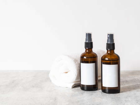 Two brown glass bottles with white label and white towel on gray table in bathroom. Front view. copy space. Blogging minimal beauty concept, cosmetics brand packaging mock upの写真素材
