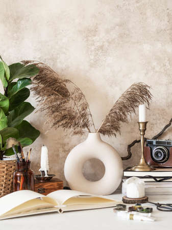 Artist's work desk with various retro objects, houseplant in pot, vase with dry reeds and open drawing pad and paints ready to workの写真素材